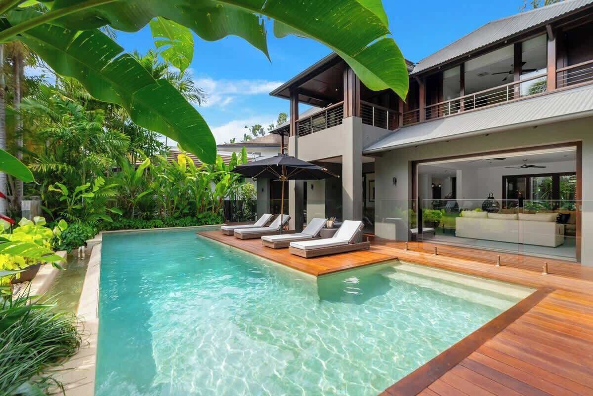 A modern pool area with clear water, wooden decking, and lounge chairs.