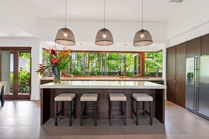 Una cucina moderna con isola centrale, illuminazione a sospensione e vista su un lussureggiante spazio verde.