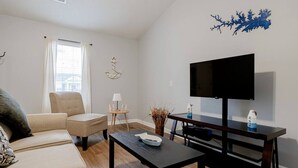 Ett vardagsrum med en soffa, ett soffbord, en tv på ett tv-bord, ett litet sidobord med en lampa och en dekorativ väggdekoration.