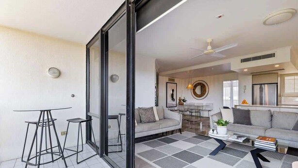 A modern living room with a sofa, coffee table, and a glass door leading to a balcony.