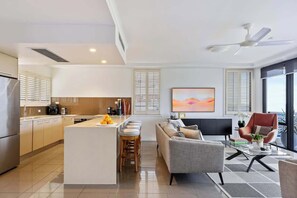 Une cuisine moderne dotée d’un îlot central, d’un coin repas avec un canapé et des chaises, et d’une grande fenêtre avec des stores.