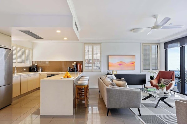A modern kitchen with a central island, a dining area with a sofa and chairs, and a large window with blinds.