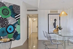 A modern dining area with a glass table, metal chairs, a decorative wall with abstract patterns, and a pendant light.
