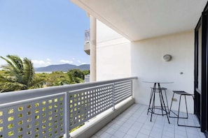 A balcony with a white railing, two small tables, and a view of greenery and mountains.
