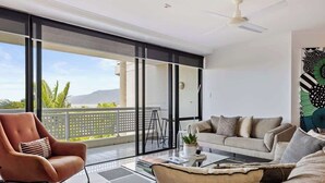 A modern living room with a sofa, armchair, and coffee table, large sliding glass doors to a balcony, and a ceiling fan.