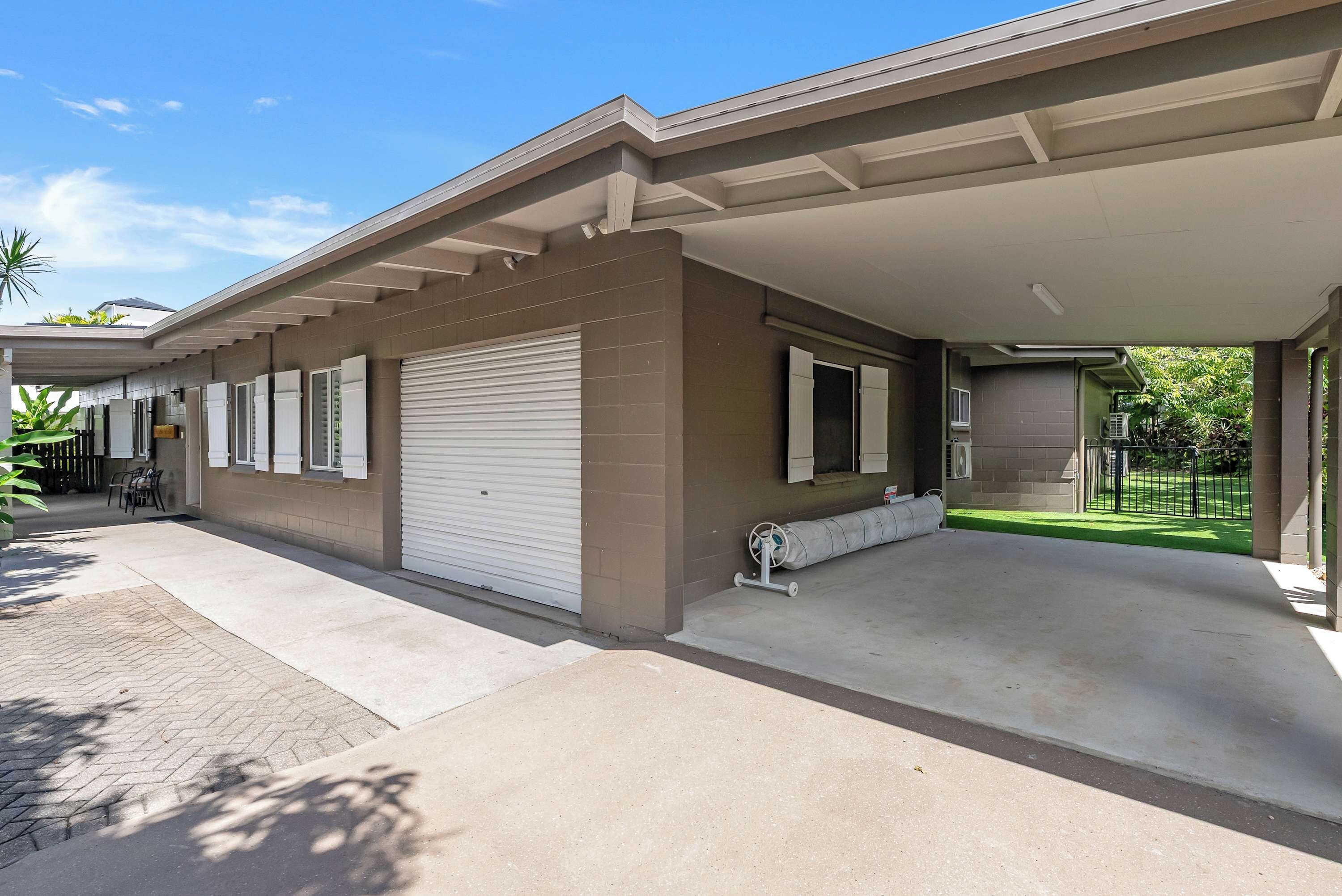 A residential property with a covered garage, a paved driveway, and a small outdoor seating area.