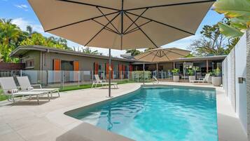 A swimming pool with lounge chairs and umbrellas, surrounded by a building with glass doors and a covered patio area.