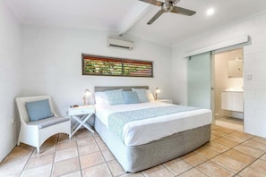 A bedroom with a bed, bedside tables, a chair, a ceiling fan, and a bathroom visible through an open door.