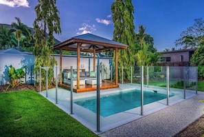 Ein moderner Poolbereich im Freien mit Glasveranda, Holzpavillon und üppiger Bepflanzung.