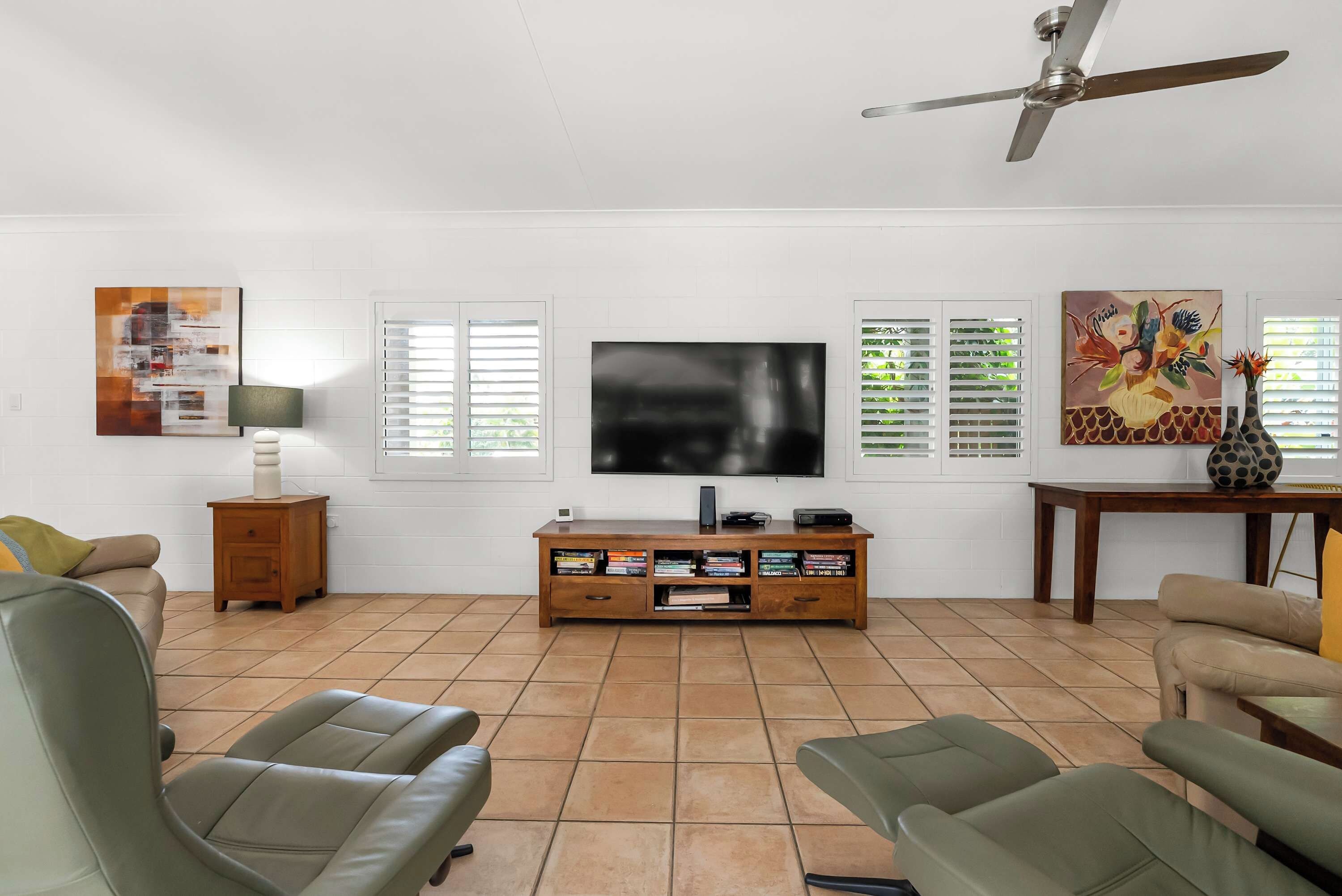 A living room with a flat-screen TV, a wooden entertainment unit, and a ceiling fan.