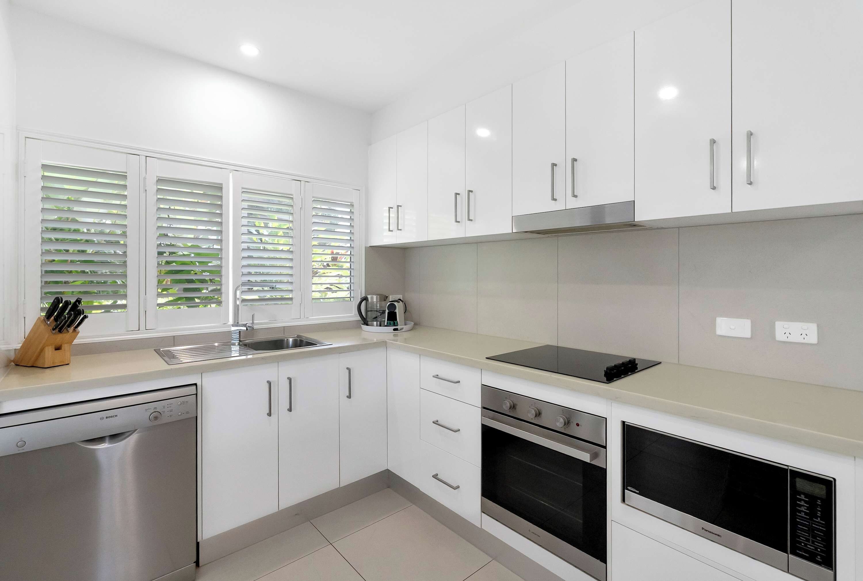 A modern kitchen with white cabinets, a Bosch dishwasher, a Panasonic oven, and a coffee maker.