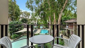 Un balcon donnant sur une piscine, entouré d’arbres et d’immeubles.