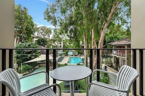 A balcony with a view of a swimming pool, surrounded by trees and buildings.