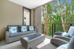 Un balcone con un divano e delle sedie, un'ampia finestra vista alberi e uno specchio fissato al muro.