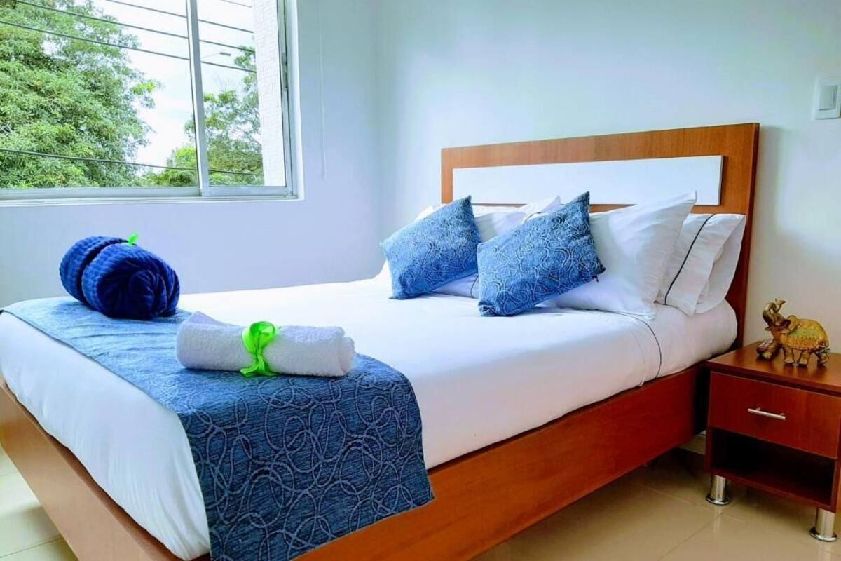 A neatly made bed with a blue patterned bedspread, white pillows, and a blue knitted item on the side.
