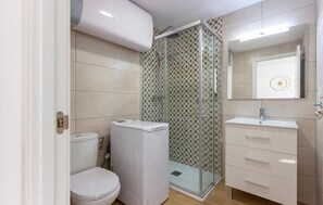 Bathroom features a toilet, washing machine, and glass-enclosed shower with a patterned tile design.