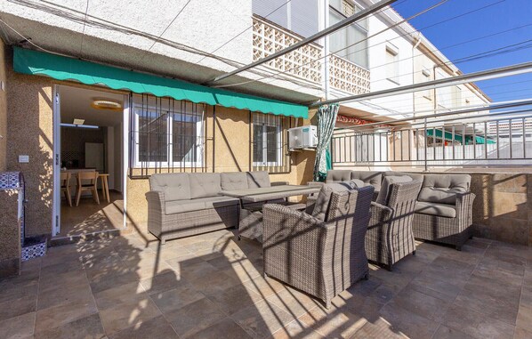 Relax on the patio with a comfortable sofa and wicker chairs, shaded by a green awning.