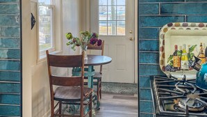 A kitchen with teal-tiled walls, a wooden dining table with chairs, a vase of flowers, and a stove with a wine-themed backsplash. - Charming Cottage (Machesney Park)