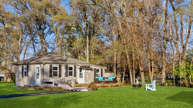 A single-story house with a front porch, a mailbox, and a small garden area with a lawn and a few trees. - Charming Cottage (Machesney Park)