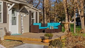 A small house with a porch, a welcome sign, outdoor furniture, and a garden with pumpkins. - Charming Cottage (Machesney Park)