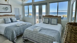 A bedroom with two beds, large windows, and a view of the ocean.