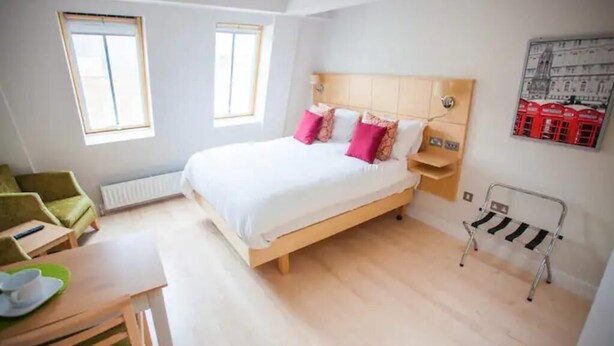 Un dormitorio con una cama de madera, dos mesitas de noche, un radiador, una silla y una estantería en la pared.