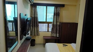 A compact hotel room with a bed, a desk, a TV, and a window with curtains.