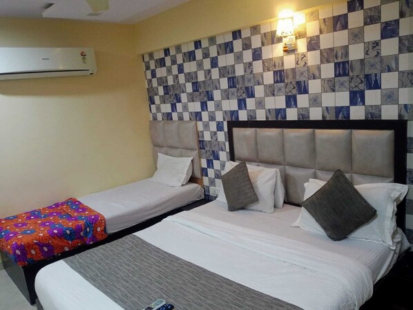A hotel room with two beds, a checkered wall, an air conditioner, and a nightstand with a remote control.