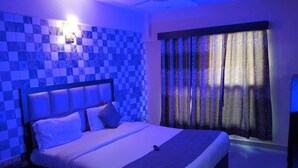 A bedroom with a checkered blue and white wall, a bed with white bedding, and a patterned curtain.