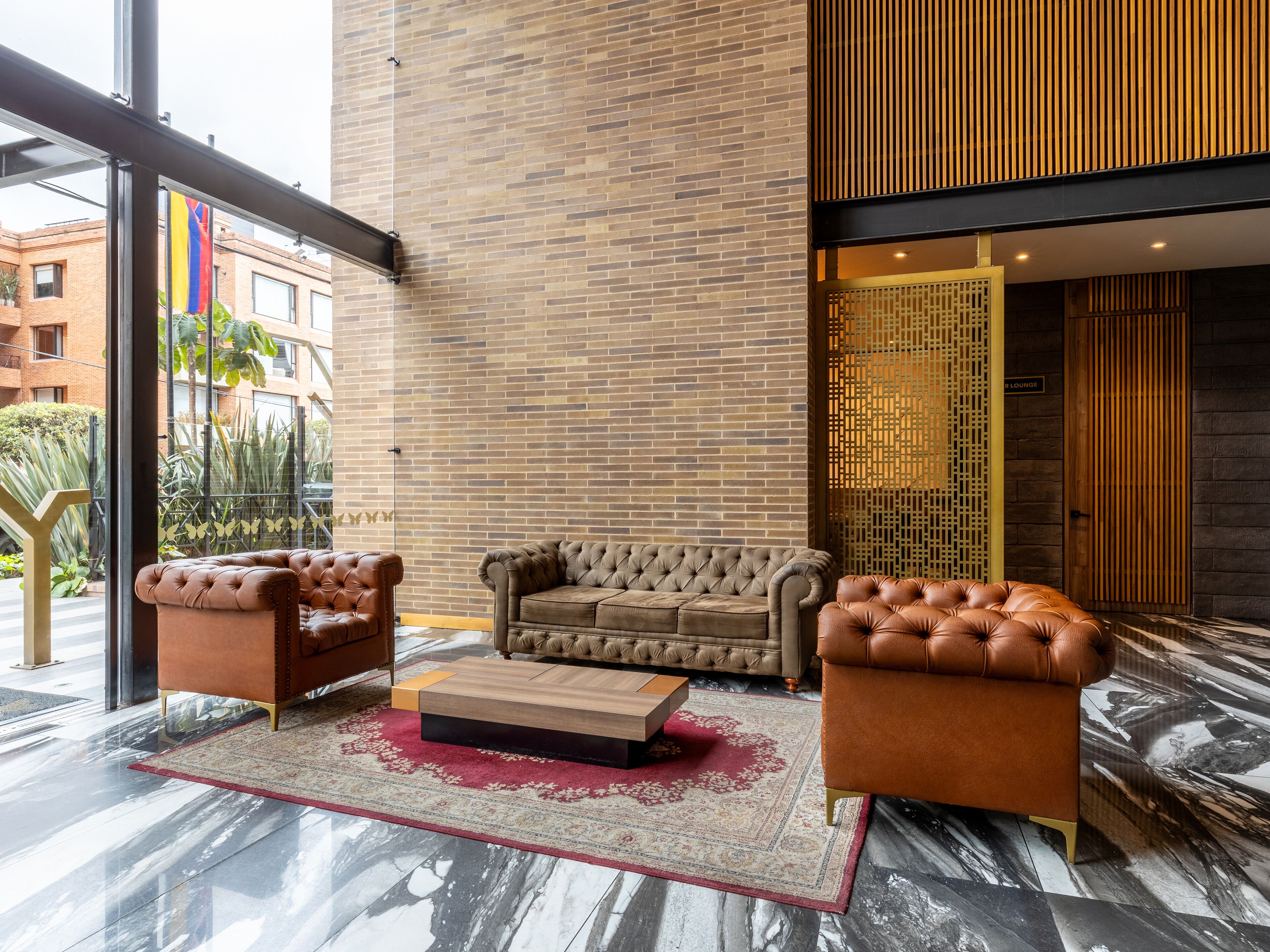A modern lounge area with a brick wall, leather sofas, and a marble floor.