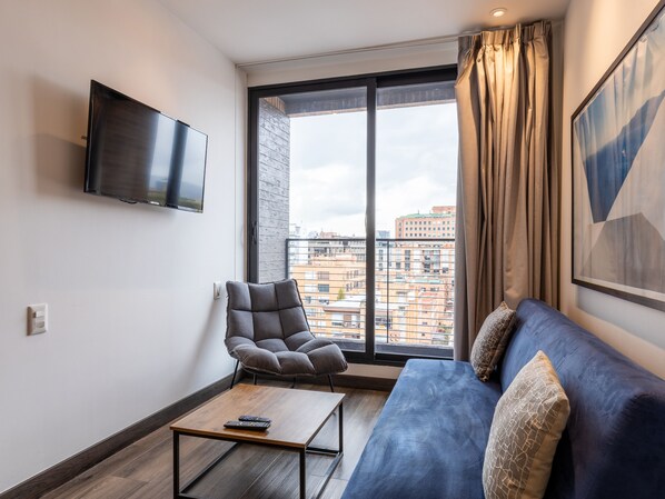 Uma sala de estar moderna com um sofá, uma poltrona, uma mesa de centro e uma TV fixada na parede.