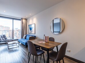 Uma sala de estar moderna com uma mesa de jantar de madeira, quatro cadeiras, um sofá e uma janela grande com cortinas.