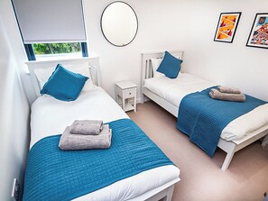 A bedroom with two beds, each with a blue bedspread and pillows, a small bedside table, and a wall-mounted mirror. - 3 bedroom accommodation in Aviemore (Aviemore)