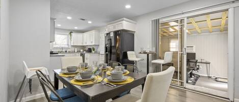 A modern kitchen with white cabinets, a large refrigerator, and a dining area with a table set for four.