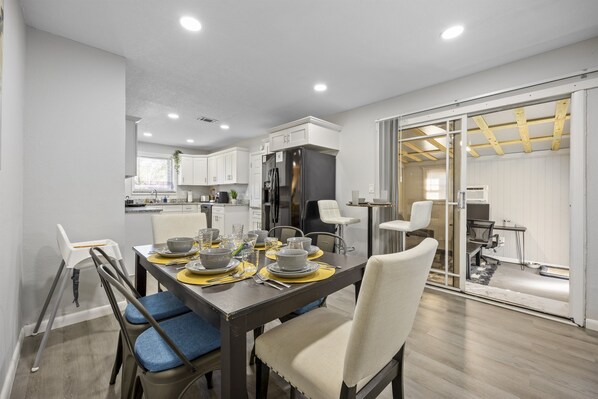 Une cuisine moderne avec des meubles blancs, un grand réfrigérateur et un coin repas avec une table dressée pour quatre personnes.