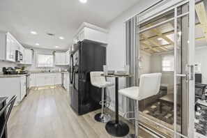Une cuisine moderne avec des meubles blancs, un réfrigérateur noir et deux tabourets de bar blancs.