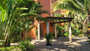 A courtyard with a pergola, palm trees, and a building with balconies. - 1 Bedroom Condo with Incredible Ocean View in Nayarit Jungle #404 (El Divisadero)