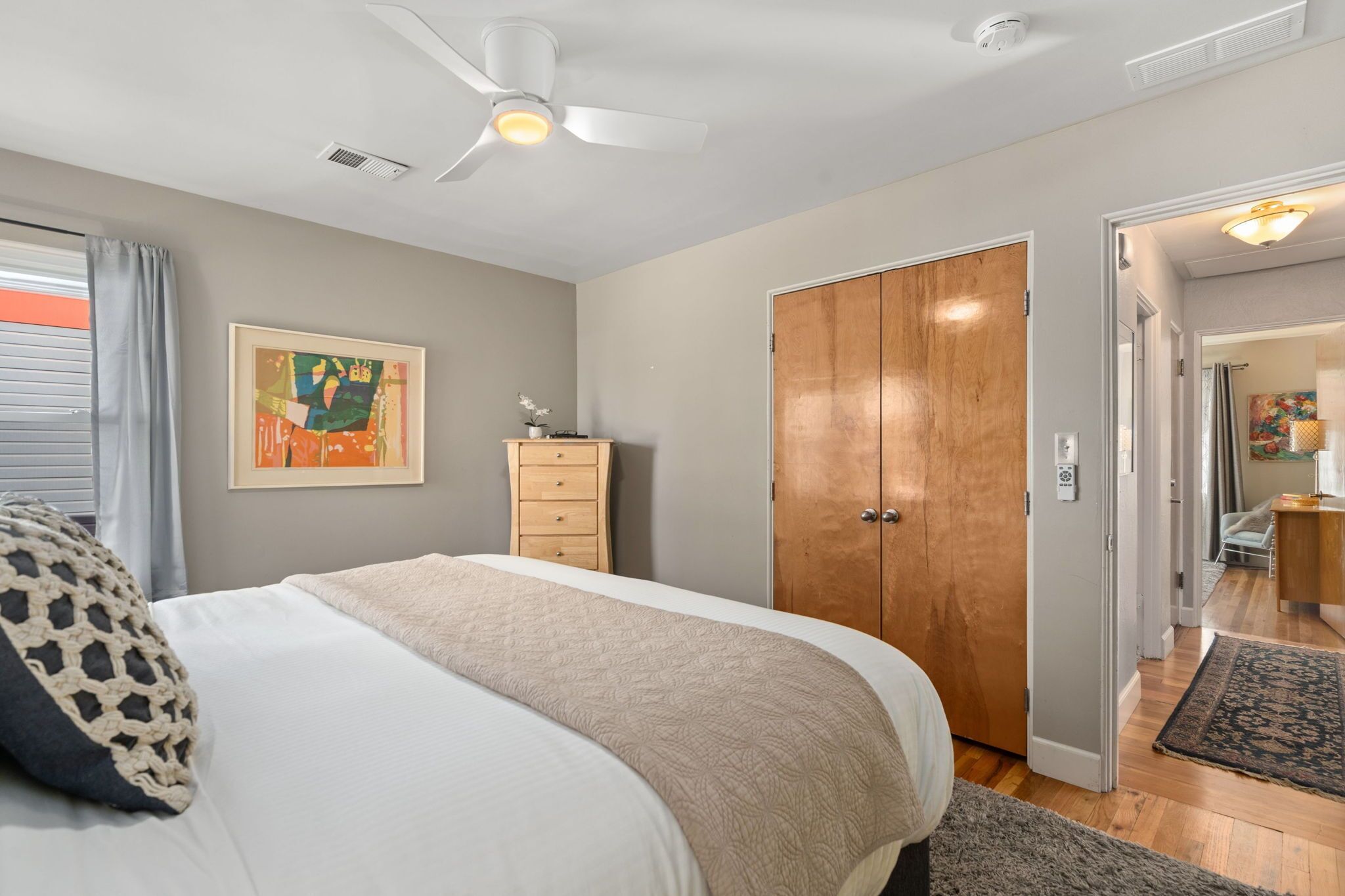 A bedroom with a bed, a ceiling fan, a wooden wardrobe, and a door leading to another room.
