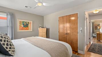 A bedroom with a bed, a ceiling fan, a wooden wardrobe, and a door leading to another room.
