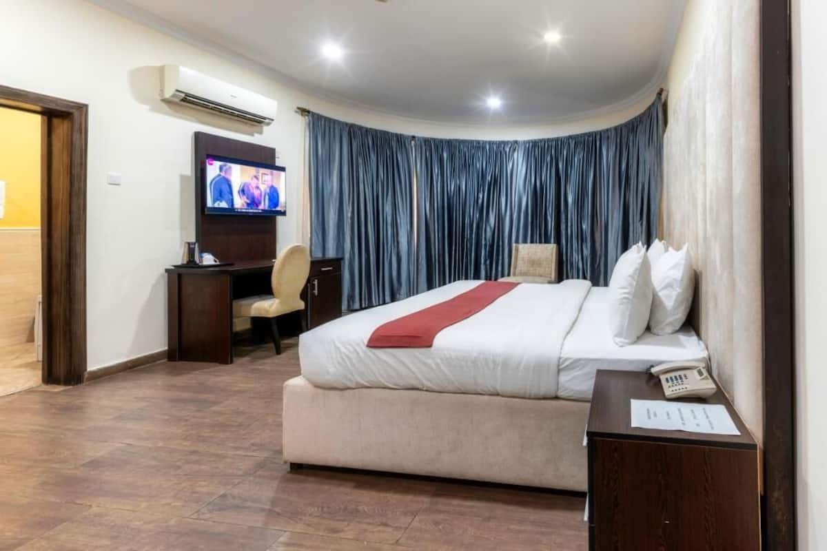 Una habitación de hotel con cama, escritorio, silla, televisor y cortina.