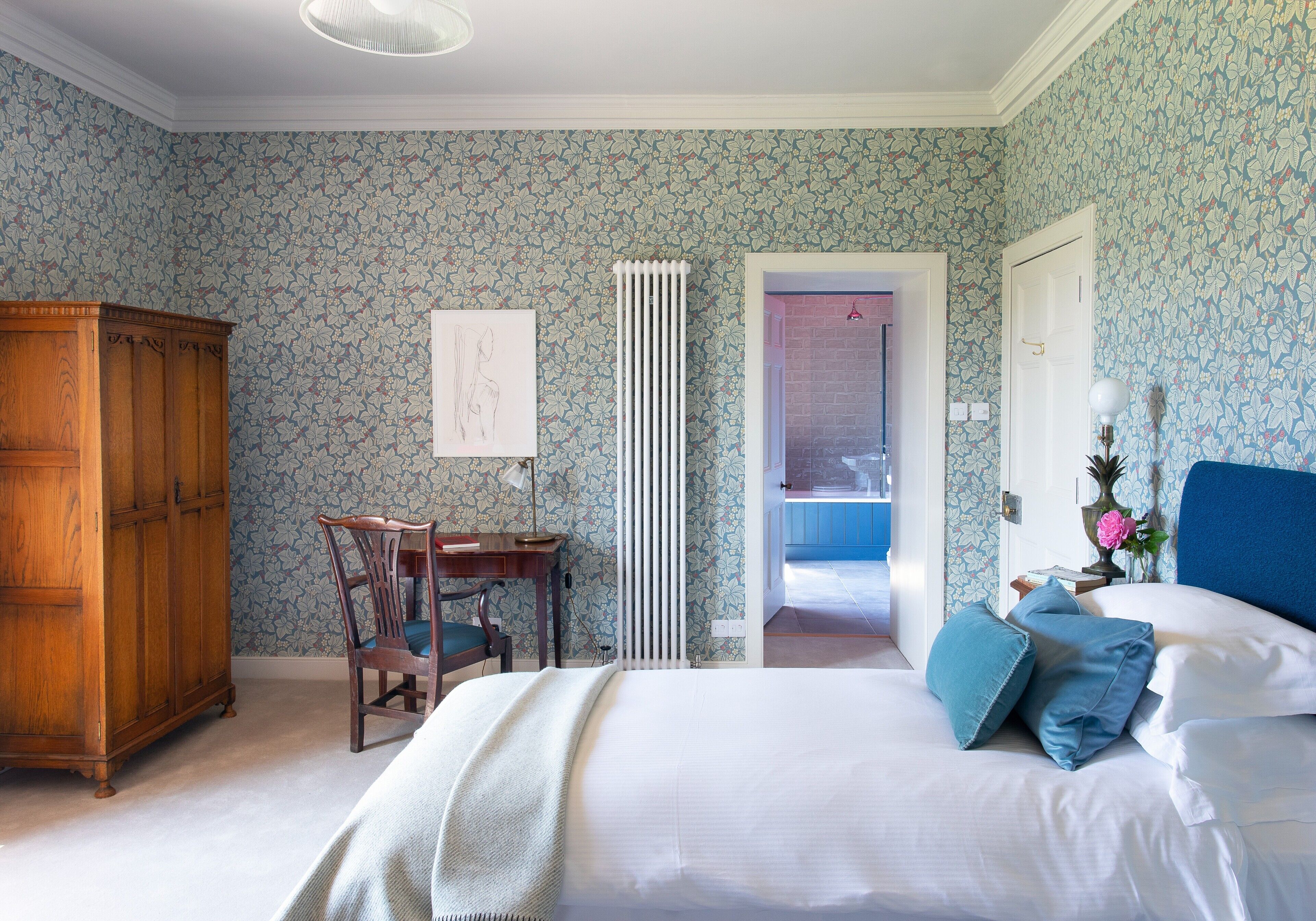 A bedroom with a large bed, a wooden wardrobe, a desk with a chair, and a radiator.