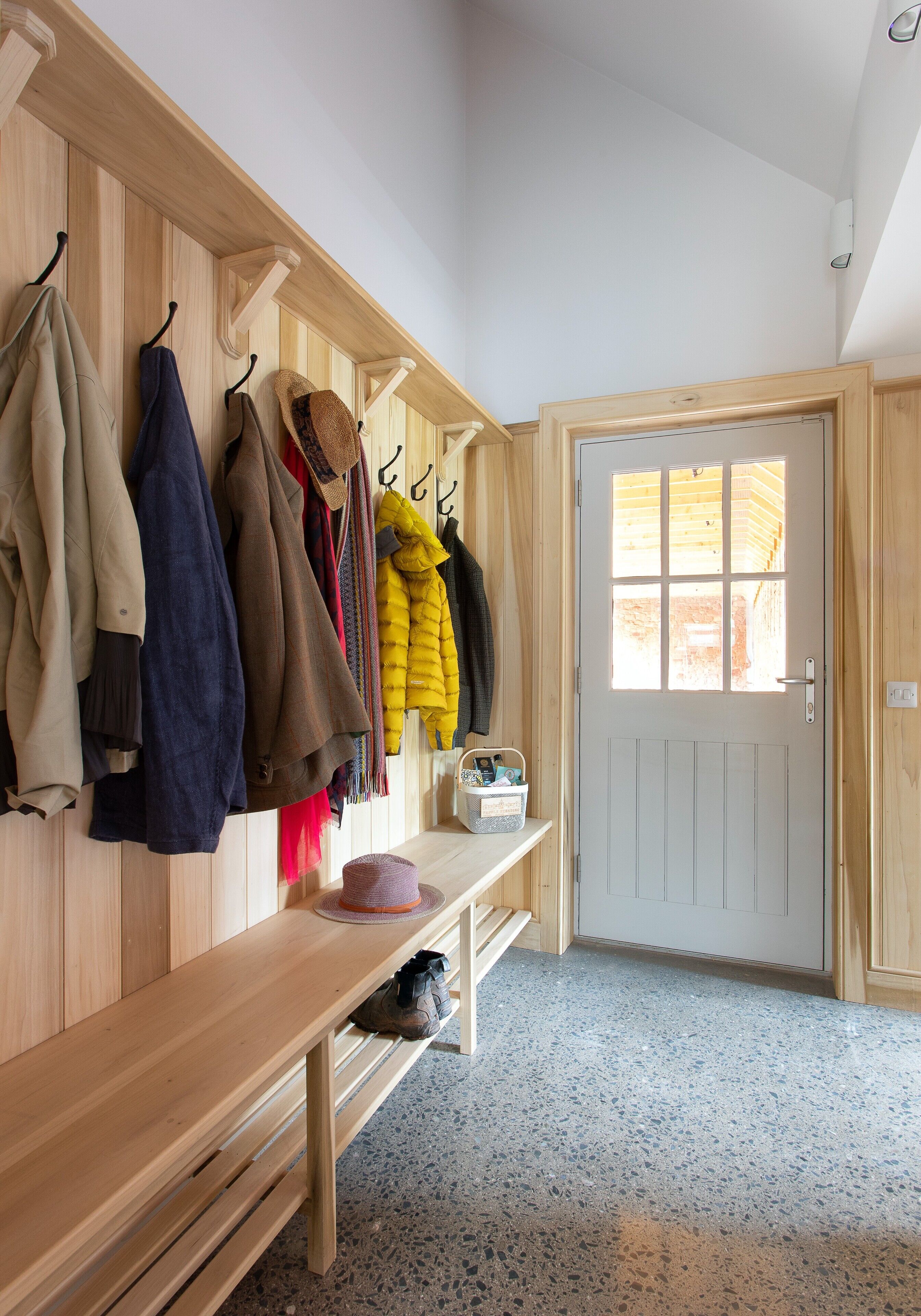 A wooden hall with coats hanging on hooks, a bench, and a door with a window.