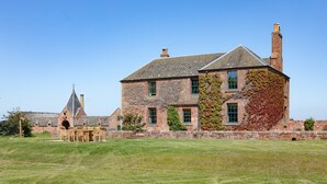 A large stone building with multiple chimneys, a prominent tower, and a well-maintained lawn in front. - Idyllic setting for large family get-togethers, groups of friends, and corporate retreats. (Haddington)