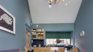 A modern living room with a purple sofa, wooden dining table, and a kitchen in the background. - Nestled in expansive grounds, this rural retreat is a sanctuary for couples and solo adventurers. (Haddington)