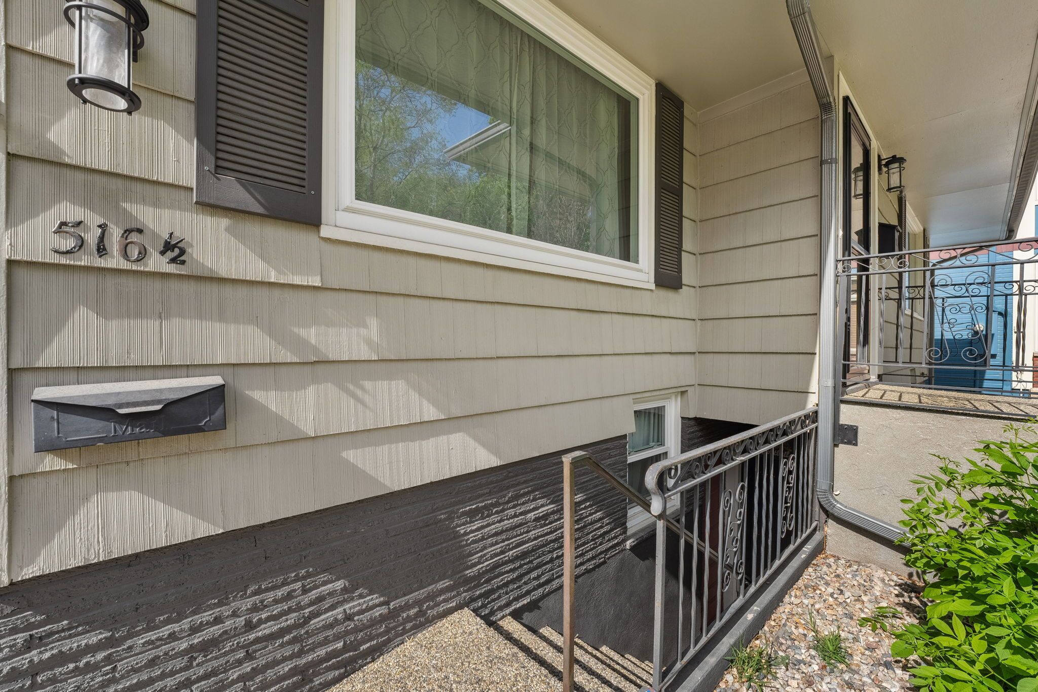 A building with a mailbox, a window with blinds, and a metal railing.