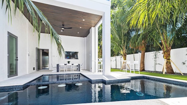 A modern outdoor pool area with a covered seating area and a view of the surrounding garden.