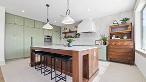 A modern kitchen with a central island, bar stools, a wooden cabinet, and pendant lighting.