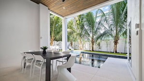 A modern outdoor dining area with a pool, white chairs, and a dark table.