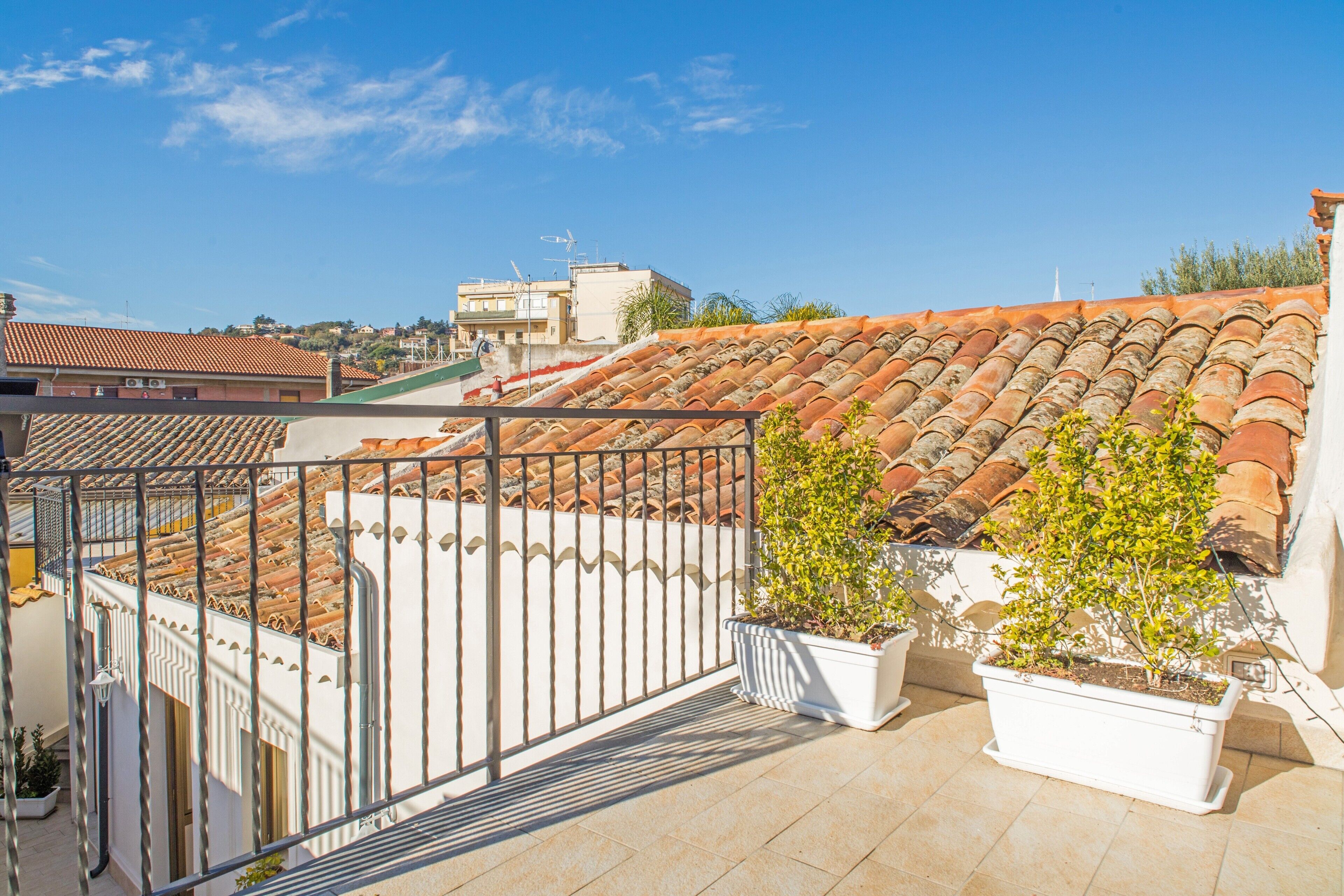 Eine Dachterrasse mit Terrakotta-Fliesen, einem Metallgeländer und Kübelpflanzen.