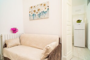 Una stanza con un divano color beige, una decorazione floreale rosa e un quadro raffigurante fiori bianchi con dettagli blu sulla parete.